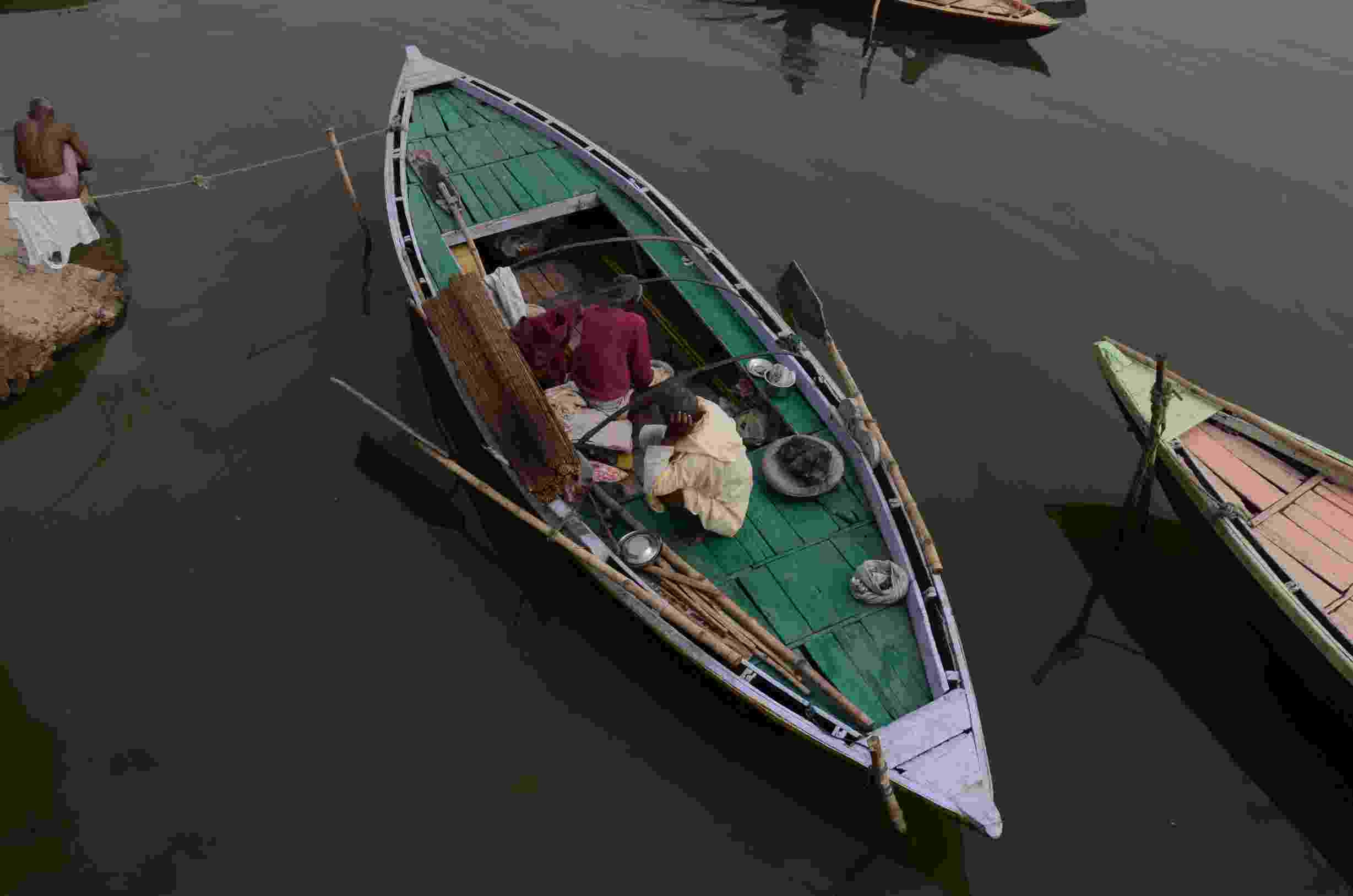 Image shows two local boatmen of Varanasi pictured from above, in their green rowing boat on the River Ganges